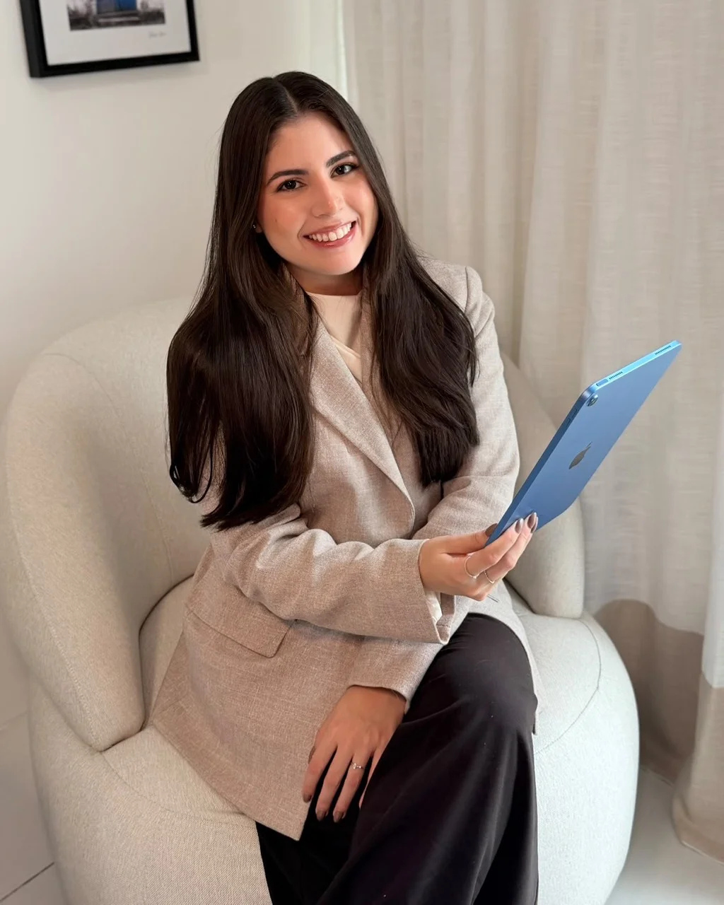 Steffanie Vasconcelos sentada, de blazer claro, segurando um tablet.